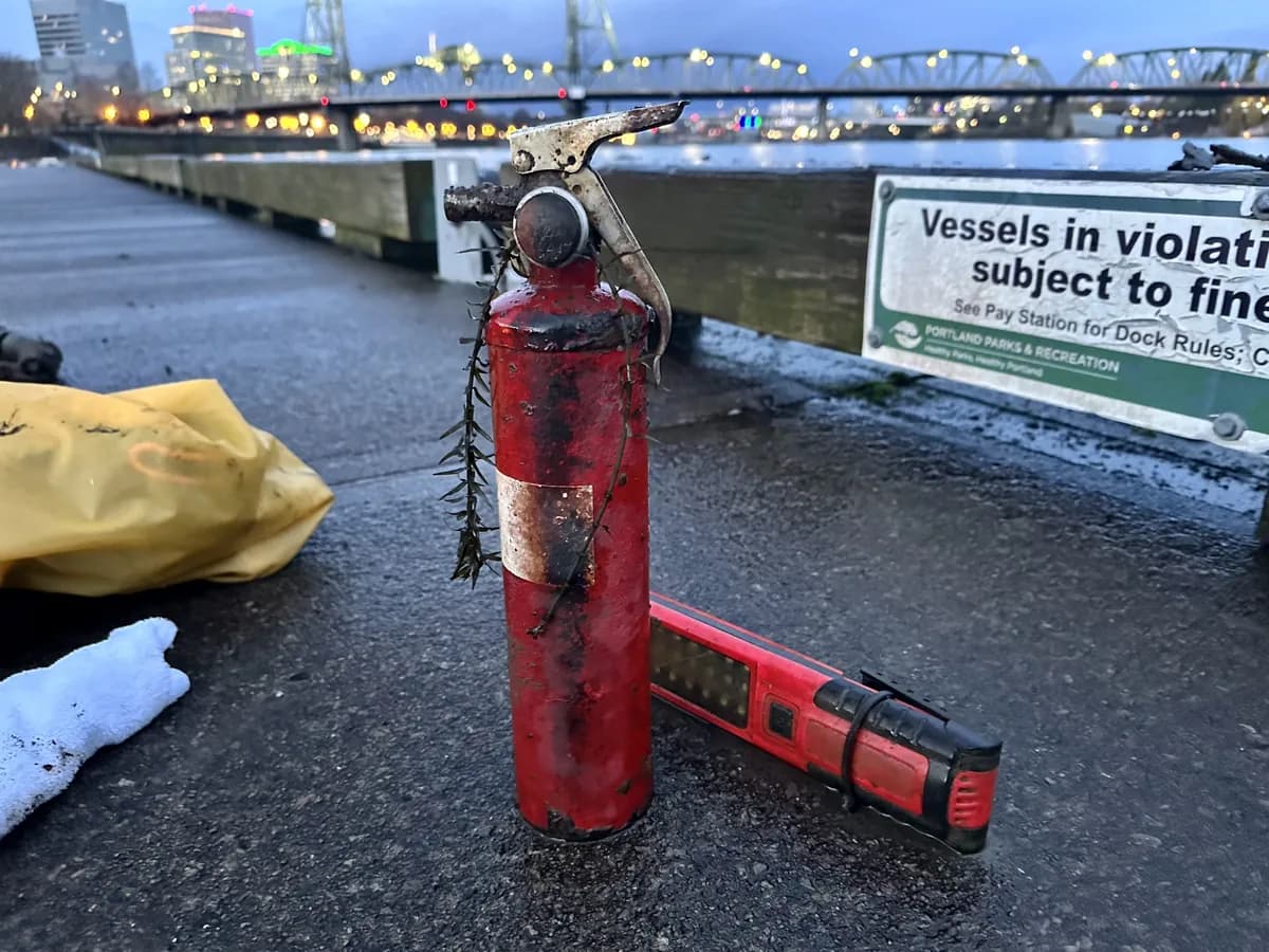 A rusty fire extinguisher and flashlight on the dock with the Portland skyline behind